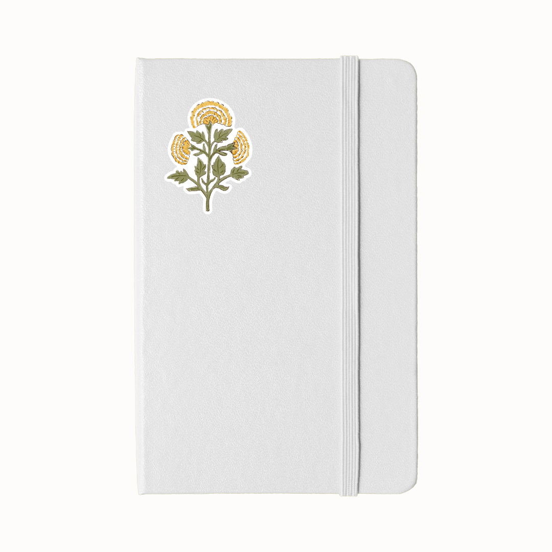 A white hardcover notebook with an elastic closure band and a yellow marigold sticker on the upper left front cover, shown against a plain white background.